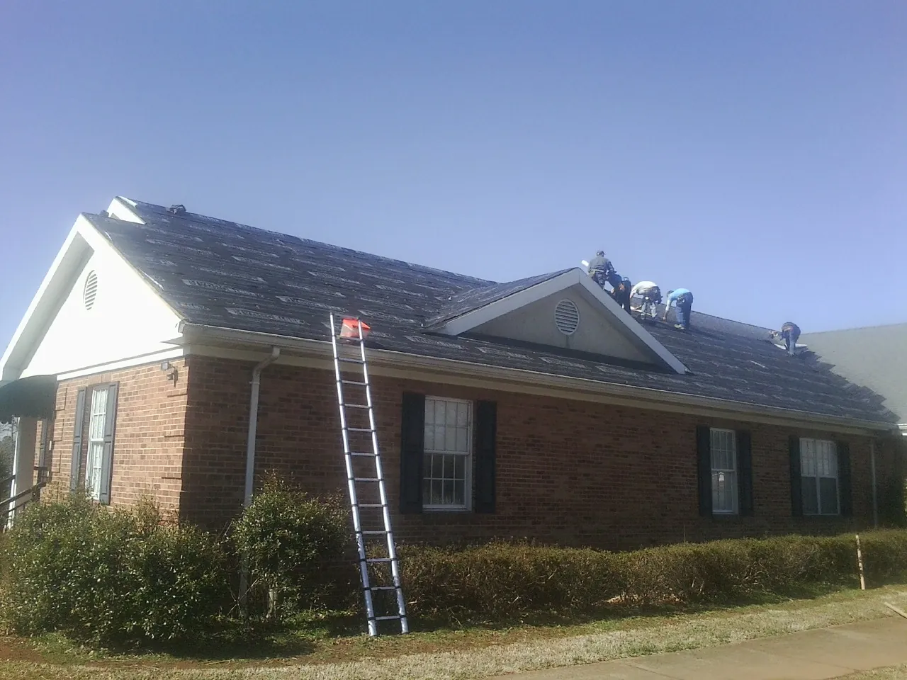 Crew tearing shingles off a brick ranch roof with a ladder set — Emergency Roof Repair work by our crew in Honey Brook