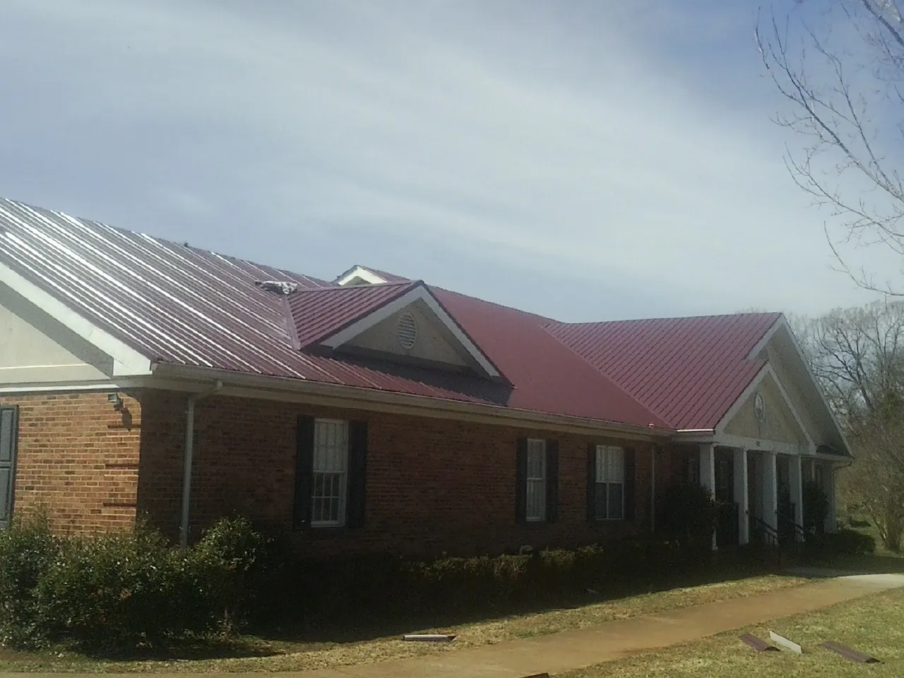 Red metal roof with gabled entries on a long brick building, from a Hail Damage Roof Repair job in Honey Brook