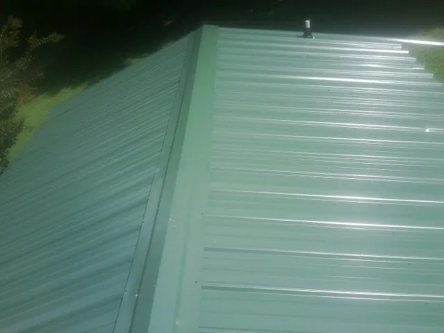 New green metal panels meeting at the ridge of a roof — Flat Roof Repair work by our crew in Honey Brook