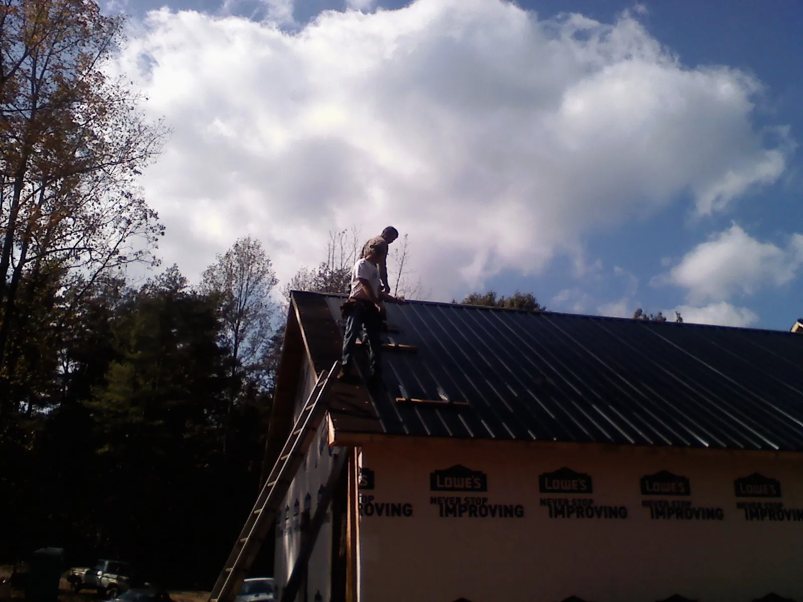Roofer fastening dark metal panels high against a cloudy sky, from a Roof Inspection job in Honey Brook