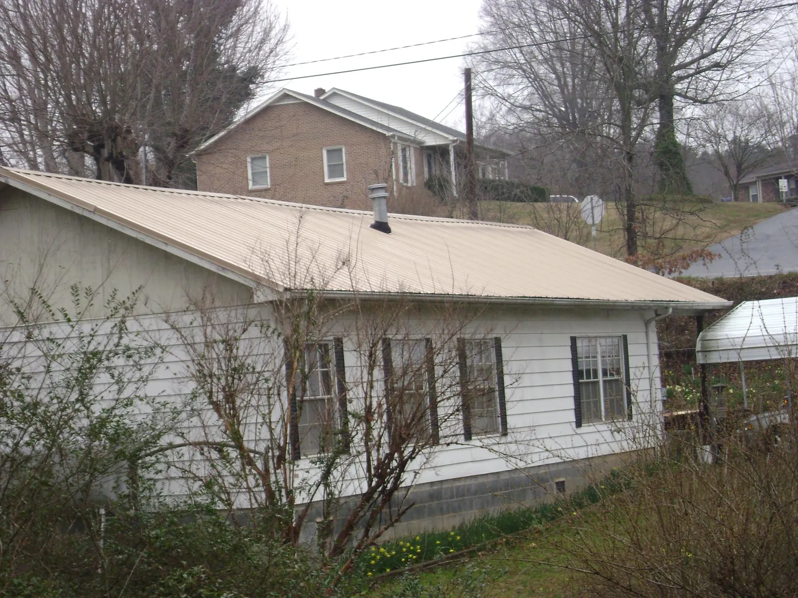 Tan metal roof on a white sided house set into a hillside — Commercial Roofing by Roofing Brothers in Honey Brook